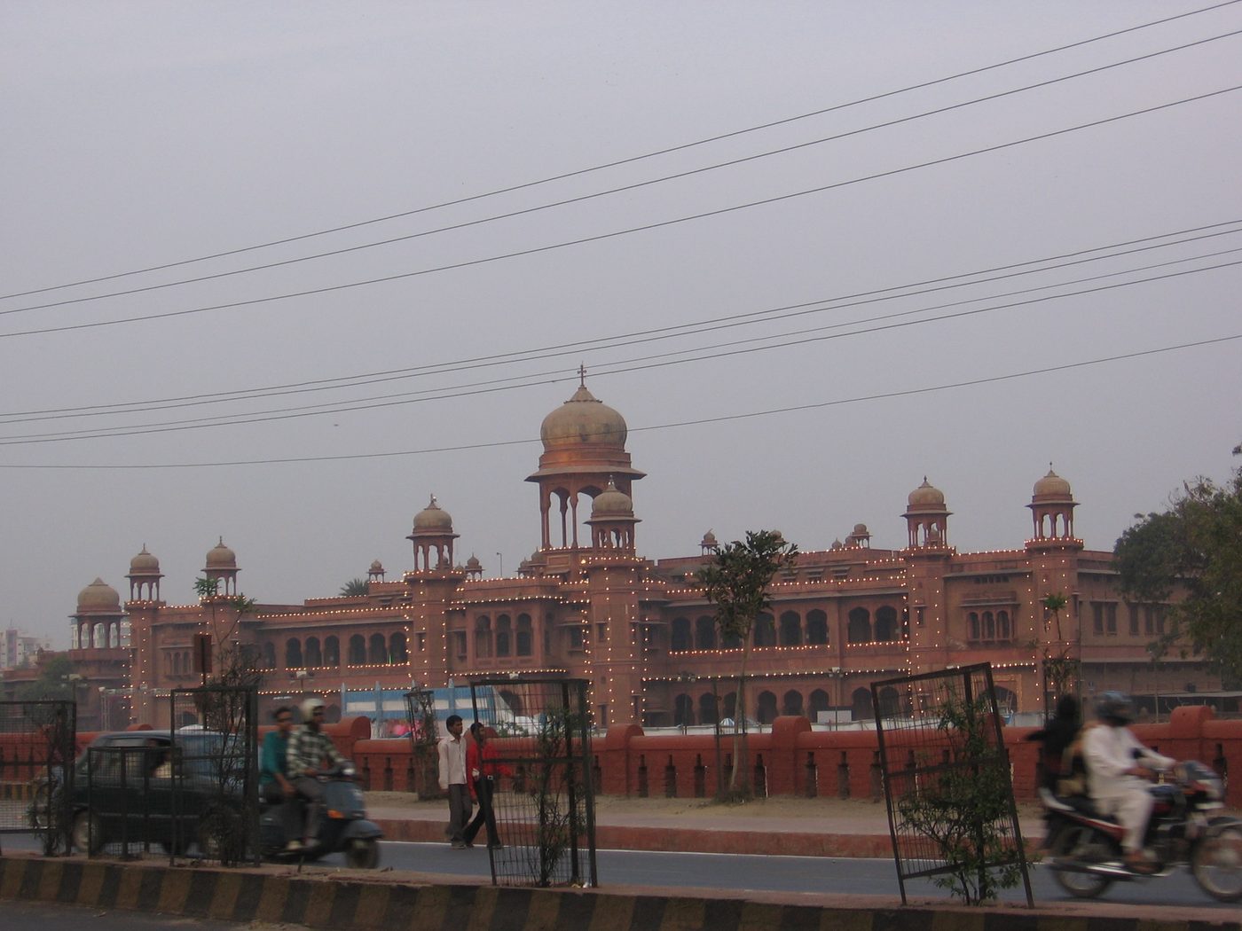 A college building lit up in the evening with students and traffic outside