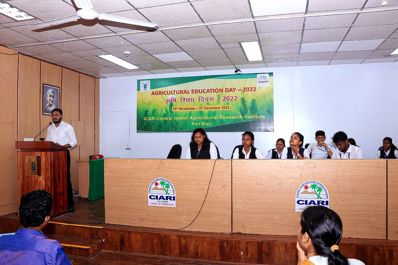 Students seated on a dais while a speaker addresses a college hall